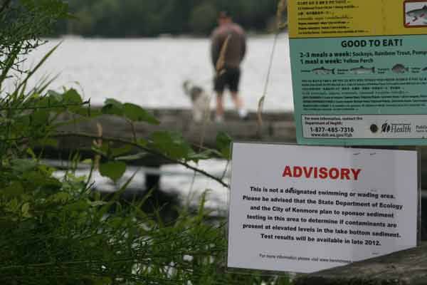 A man and his dog walk on the Log Boom Park pier last Friday while an advisory sign states that sediment testing is planned.