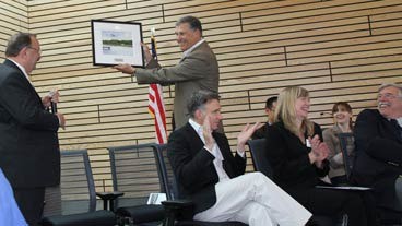 Kenmore Mayor David Baker presents Congressman Jay Inslee with a watercolor painting titled “Morning at Log Boom Park” by Kenmore artist Charlene Collins Freeman at the new City Hall dedication ceremony last Saturday. The program featured a performance by the Inglemoor High marching band.