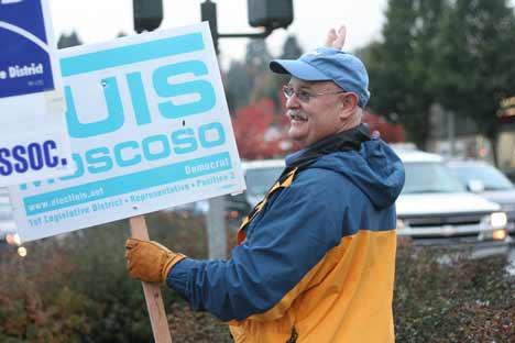 Keith Bankston raises an election sign and waves at drivers in downtown Bothell on the morning of Oct. 29.