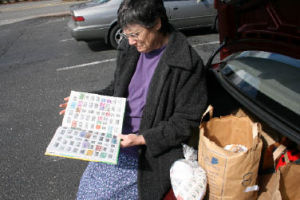 Bothell Sons of Norway member Sue Waldrop browses a stamp collection while sitting with a trunk load of used stamps that her club will eventually send to Norway to provide funding for tuberculosis research and assisting handicapped children.