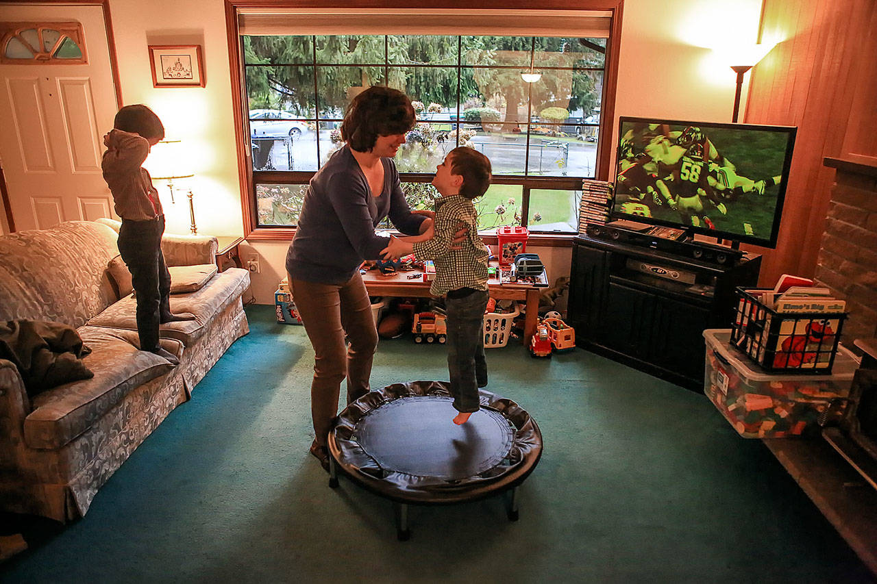 Ian Fisher watches a game as his mother, Deanna Fisher, plays with her youngest autistic son, Colin Fisher, 4, at their home in Bothell. The Fishers are volunteering baby teeth for a national study to determine if prenatal exposure to chemicals increases a child’s chances of developing the autism. (Kevin Clark / The Herald)