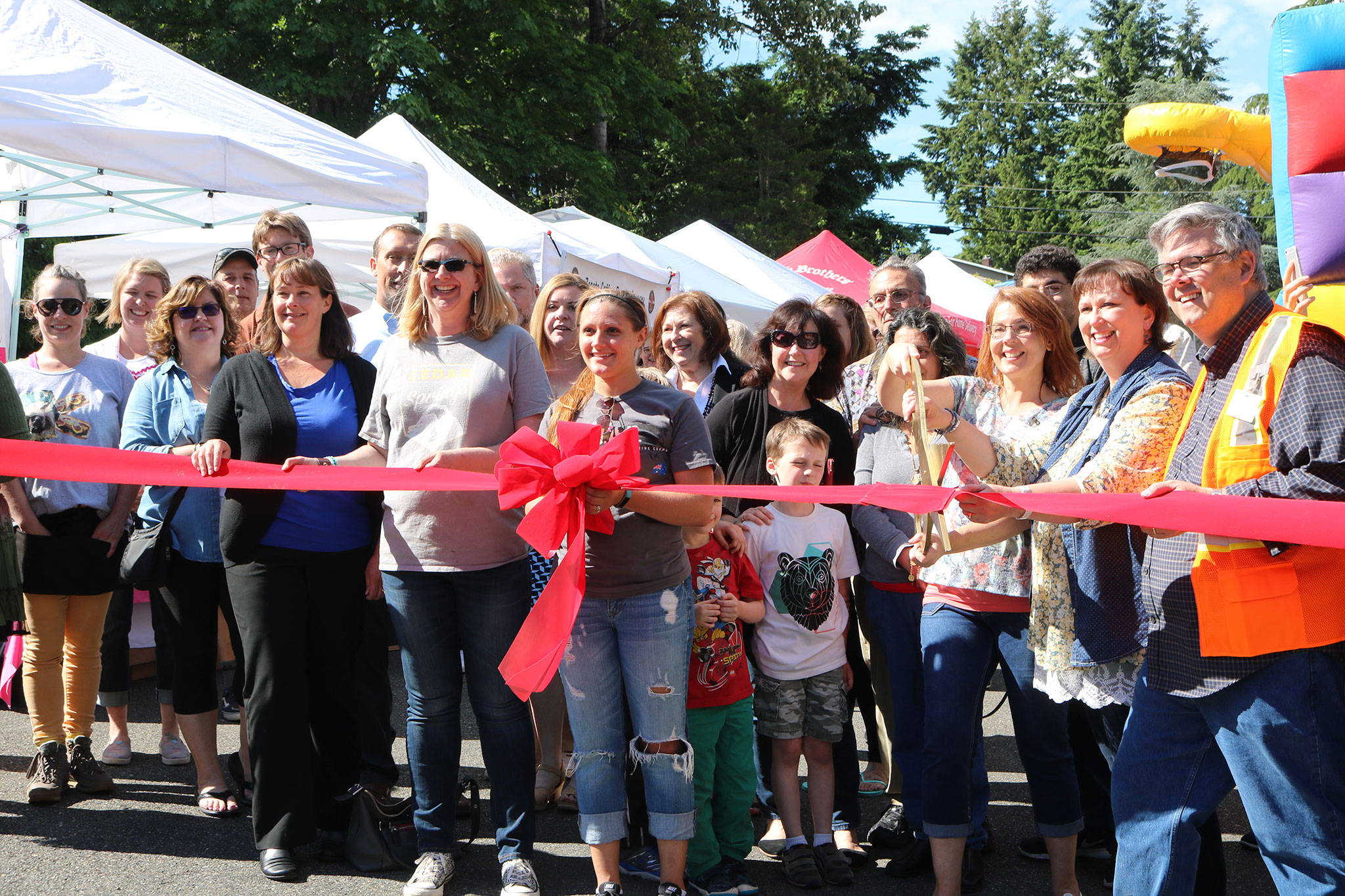 Kenmore Community Market manager Jenni Jensen (with the scissors) prepares to cut the ribbon to celebrate the market’s opening alongside city officials, Cedar Park Northshore representatives, vendors and other community members. CATHERINE KRUMMEY / Bothell-Kenmore Reporter