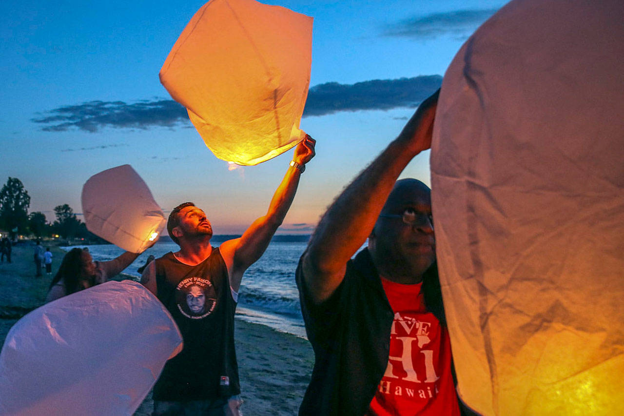 Nick Craig (left) and Pastor Donald Johnson join friends and family members of Henry Faison as they release lanterns on Alki Beach. (Kevin Clark / The Herald)