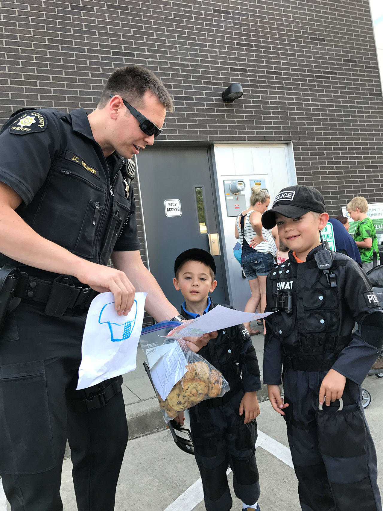 King County deputy Jeff Helmer (left) admires drawings from brothers Sam Chapman, 5, and Gabe Chapman, 8 of Woodinville. Samantha Pak, Bothell-Kenmore Reporter