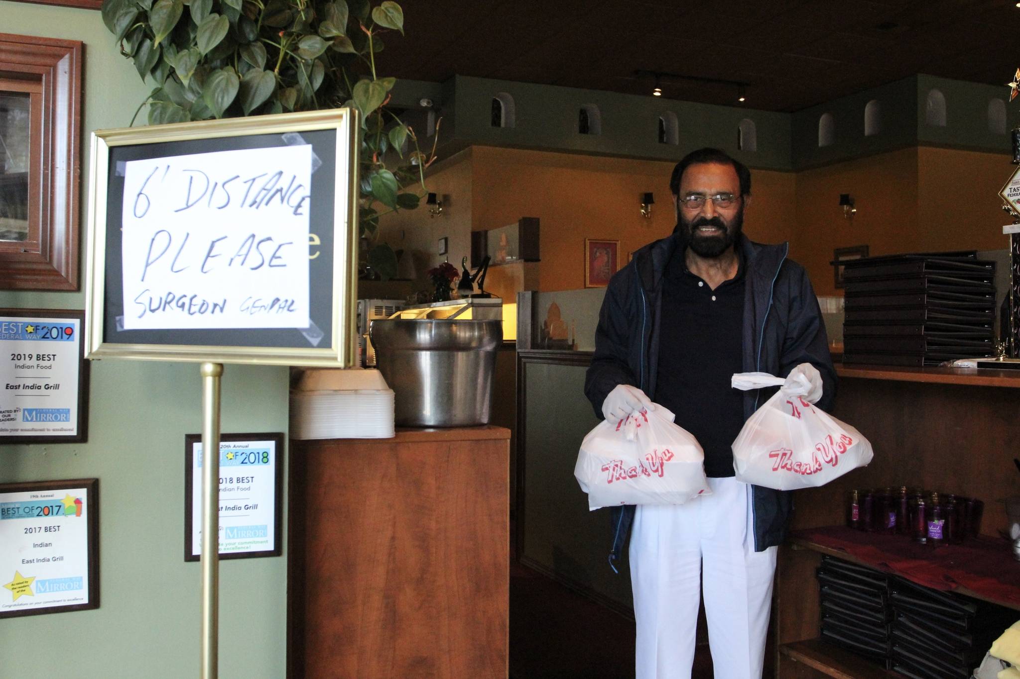 Kabal Gill, owner of East India Grill in Federal Way, wears gloves to hand over take-out orders at his restaurant on March 23. File photo