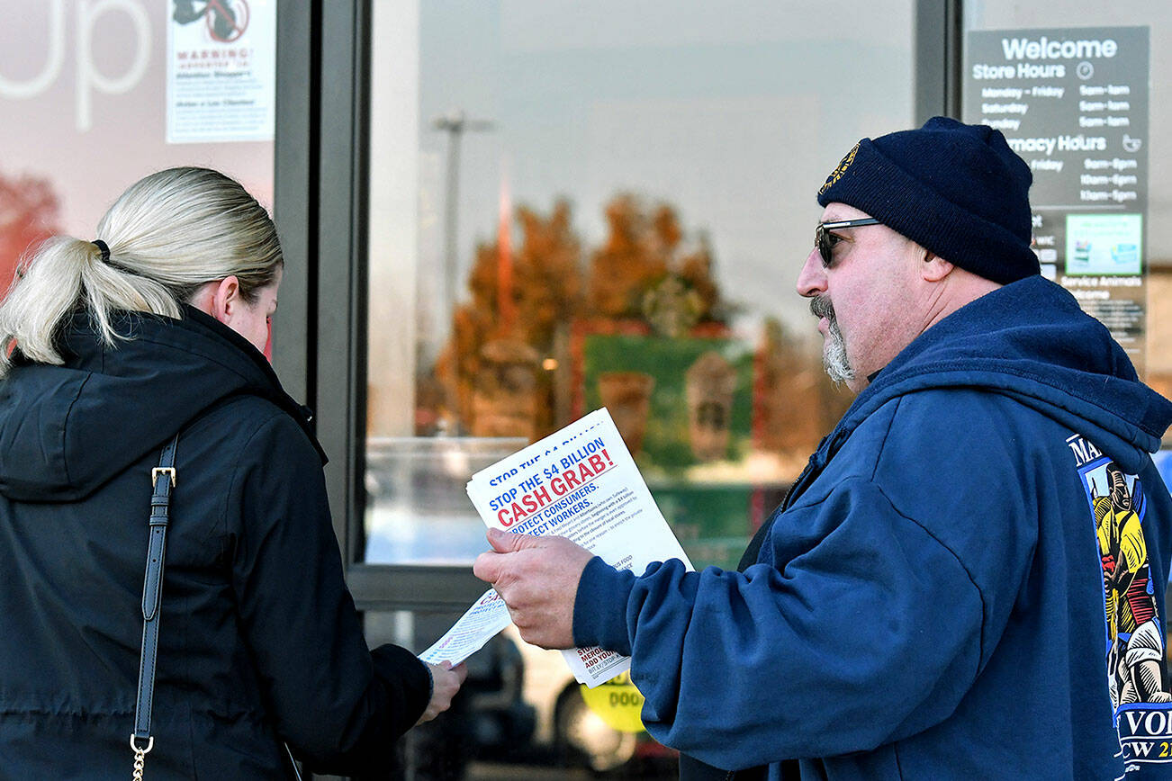 Kevin Flynn, right, a meat-cutter with the Marysville Albertsons, hands a leaflet to a shopper during an informational campaign on Wednesday, Nov. 9, 2022. Flynn was one of about a dozen grocery store workers handing out leaflets to shoppers about the proposed merger between Albertsons and Kroger. (Mike Henneke / The Herald)