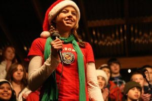 Kenmore Junior High symphonic choir member Anna Radavich smiles at the crowd during a break in her solo Saturday night at Country Village's holiday tree-lighting and Santa-arrival event in Bothell.