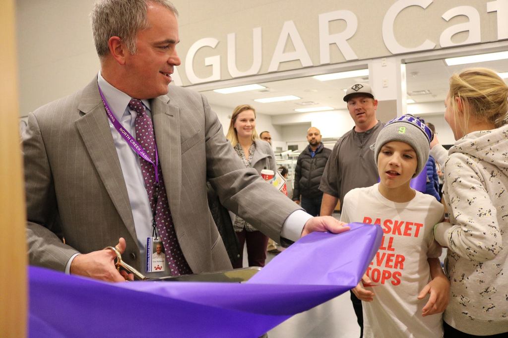 North Creek High School Principal Eric McDowell cuts a piece of ribbon for a young visitor during the open house on Nov. 21. The ribbon went quickly, as scores of onlookers crowded around for a slice. JOHN WILLIAM HOWARD/Bothell-Kenmore Reporter