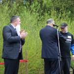 As part of being named Washingtonian of the Day, Gov. Jay Inslee (center) gives David Bain (right) the Washington State pin from his lapel. Bothell Mayor Andy Rheaume (left) applauds Bain receiving the honor on behalf of all of those who contributed to the city&rsquo;s acquisition of North Creek Forest. CATHERINE KRUMMEY / Bothell Reporter