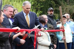 Bothell Mayor Andy Rheaume and Gov. Jay Inslee cut the ribbon to celebrate the city&rsquo;s procurement of all of North Creek Forest, surrounded by local officials and others involved in the acquisition process. CATHERINE KRUMMEY / Bothell Reporter