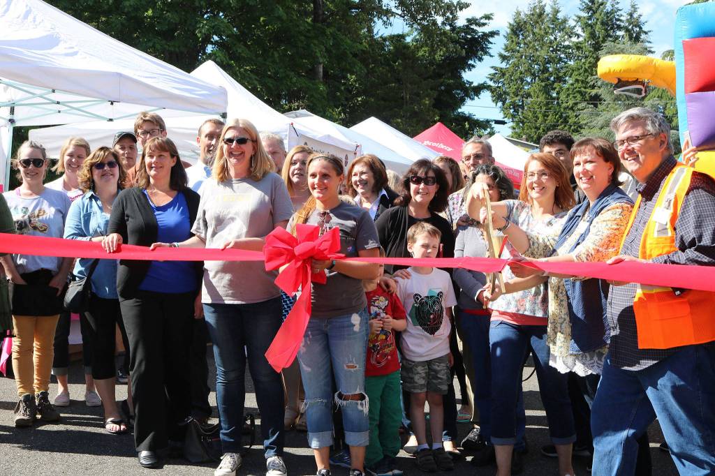 Kenmore Community Market manager Jenni Jensen (with the scissors) prepares to cut the ribbon to celebrate the market&rsquo;s opening alongside city officials, Cedar Park Northshore representatives, vendors and other community members. CATHERINE KRUMMEY / Bothell-Kenmore Reporter