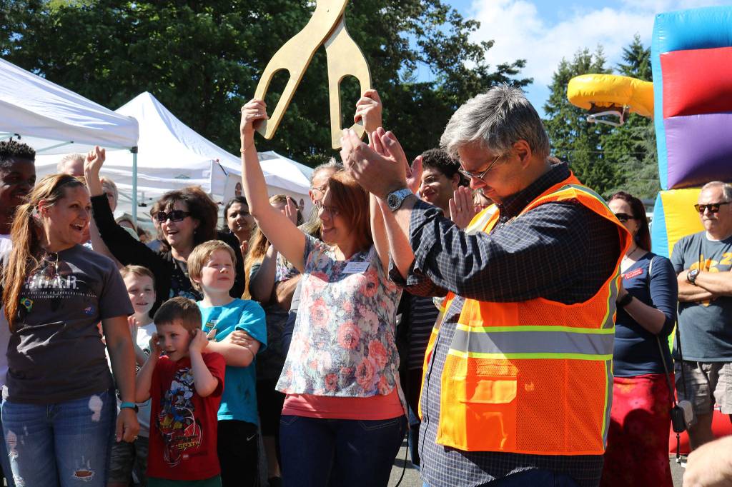 The crowd, including Cedar Park Northshore lead pastor Dan Neary (in the orange vest), celebrates after Kenmore Community Market manager Jenni Jensen (with the scissors) cuts the ribbon to celebrate the market&rsquo;s opening. CATHERINE KRUMMEY / Bothell-Kenmore Reporter